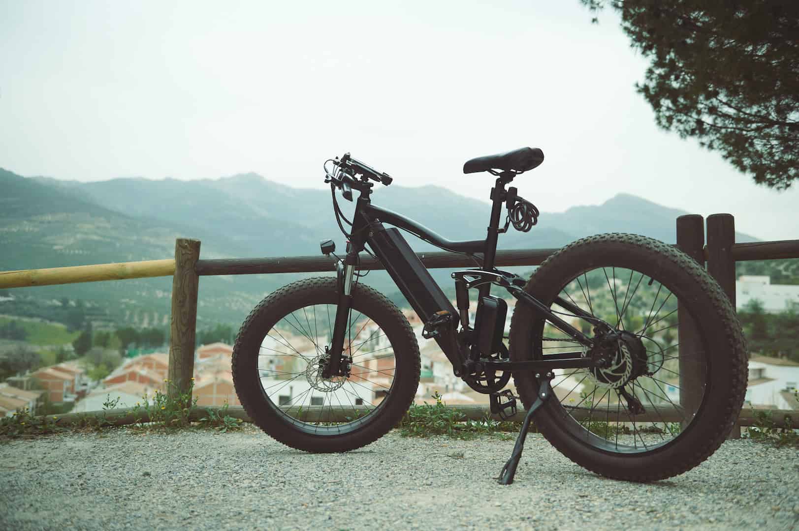 full size shot of a modern black electric bike on the countryside road parked by a wooden fence against mountains